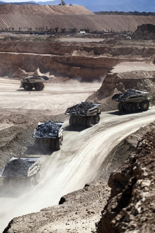 Turning mine haul road data into operational value 2 Mining haul trucks navigating a dirt mine road with large open-pit excavation in the background.